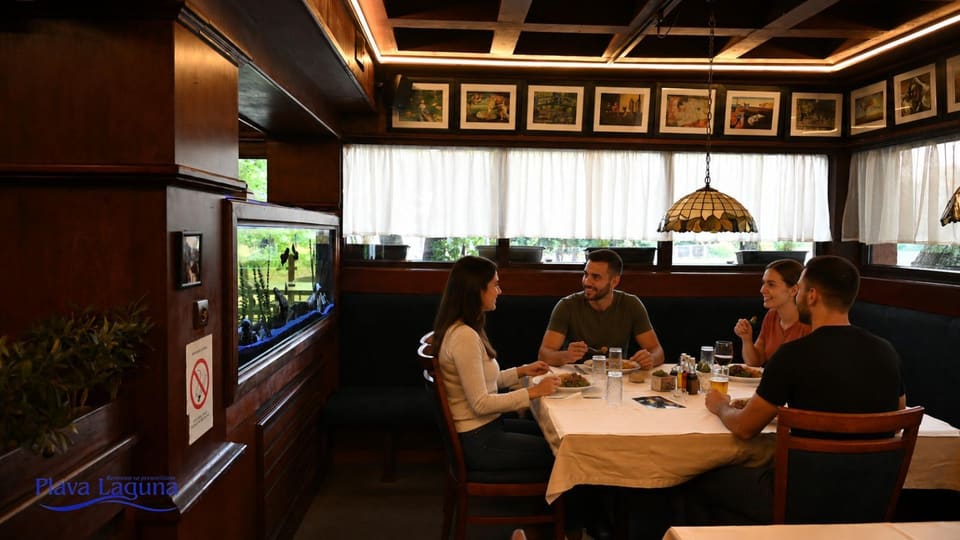 Četvoro gostiju ruča za stolom u sali, pored akvarijuma
